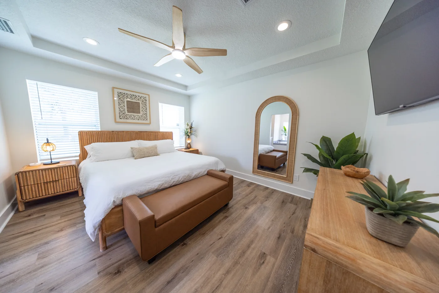 Coastal primary bedroom with rattan headboard, leather bench, and arched mirror at Adventure Acres