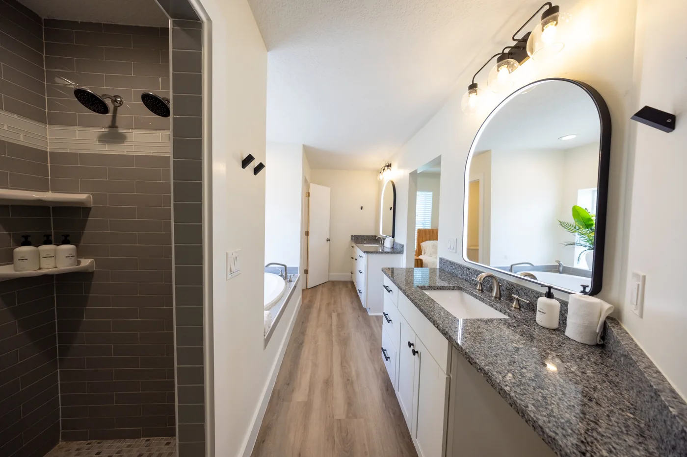 Primary bathroom with dual rainfall shower, granite double vanity, and arched mirror at Adventure Acres