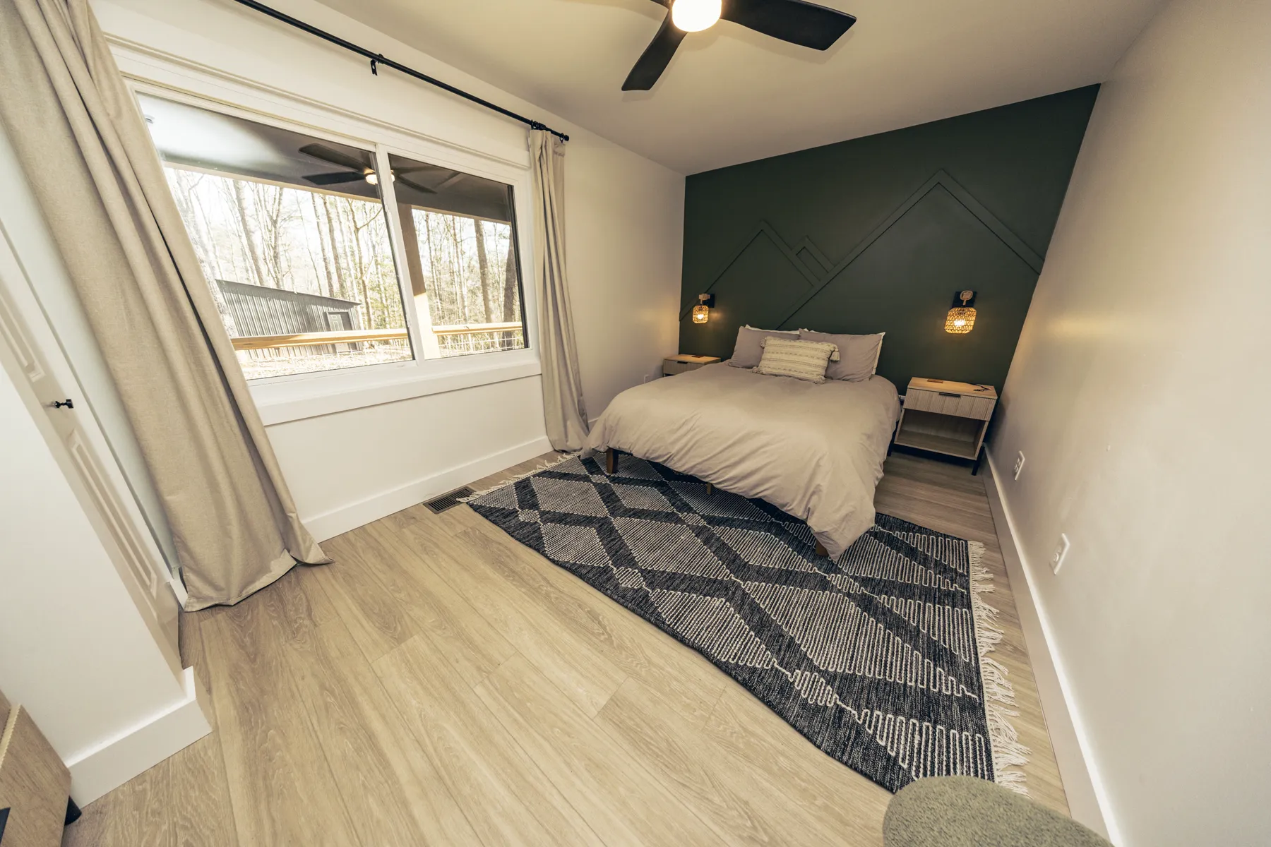 Guest bedroom at Adventure Acres with a forest-green accent wall, mountain-shaped trim, rattan sconces, and a patterned rug