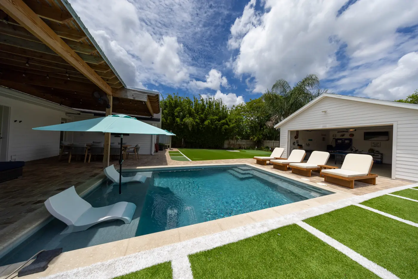 Backyard pool with lounge chairs, covered patio, and putting green at a designed short-term rental