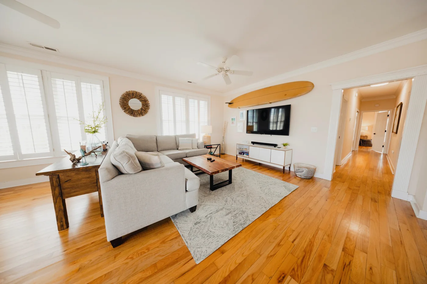 Bright coastal living room with sectional sofa, surfboard wall mount, and hardwood floors