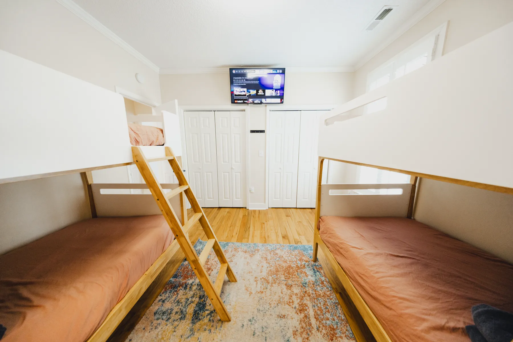 Bunk room with two sets of wooden bunk beds, a wall-mounted TV, and a colorful rug at Kailani House
